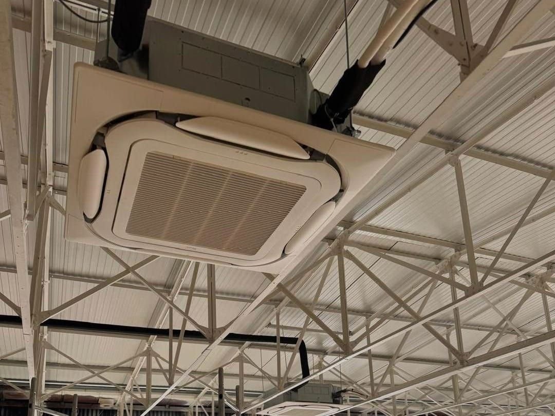 Cassette de climatisation plafonnière en cours de pose sous la charpente métallique d’un garage automobile