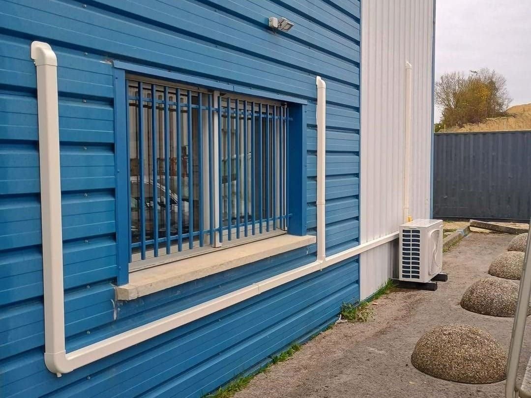 Goulotte blanche et unité extérieure de climatisation le long d’une façade en bardage bleu, dans le Var