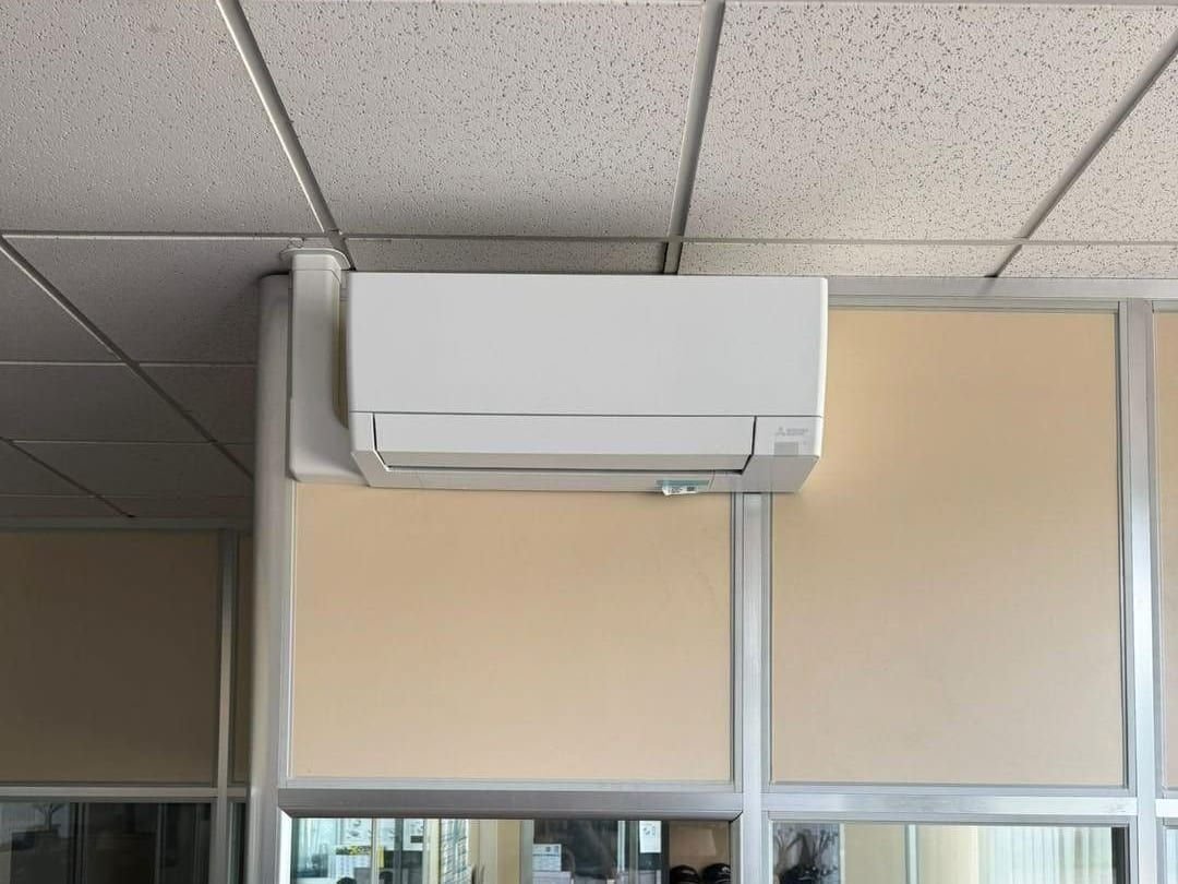 Unité intérieure murale de climatisation réversible au-dessus d’une cloison vitrée, dans des bureaux en Loire-Atlantique